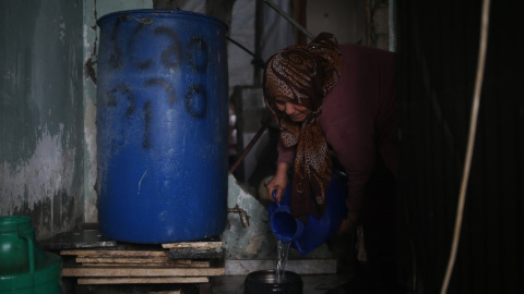 Etadal Abu Oda, una mujer palestina de 57 años de edad, toma agua de un tanque para limpiar los platos en su casa en Beit Hanoun, en el norte de la Franja de Gaza. Mohammed ABED / AFP