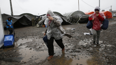 Varias personas tratan de protegerse de la lluvia en una de las tiendas del campamento de Slavonski Brod. - REUTERS