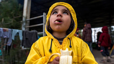 Una niña come un plátano en el campo de refugiados en Idomeni. EFE/ Georgi Licovski