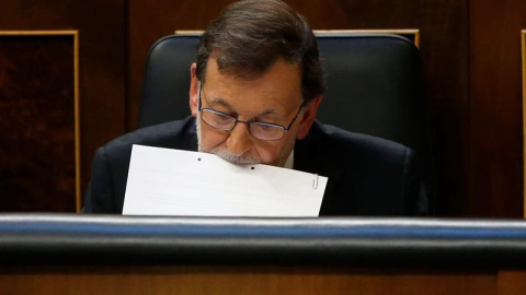 El presidente del Gobierno en funciones, Mariano Rajoy, sujeta unos papeles con la boca durante el pleno del Congreso de los Diputados donde ha comparecido hoy de forma extraordinaria y por vez primera en esta legislatura para informar de l