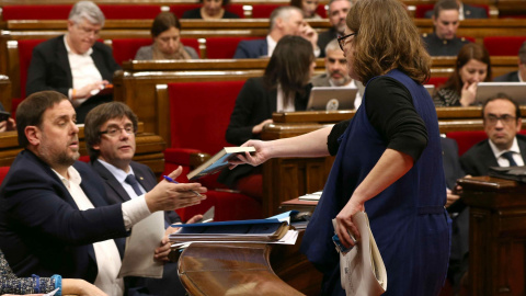 La diputada de la CUP Eulàlia Reguant le regala el libro 'L'hora dels voltors', de Josep Manel Busqueta, al vicepresidente Oriol Junqueras ante el presidente de la Generalitat, Carles Puigdemont, durante el debate de los Presupuestos de 201