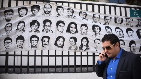 Un hombre pasa en Ciudad de Guatemala junto a un mural con rostros de desaparecidos durante el conflicto armado. - AFP