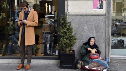 Un hombre consulta a su móvil junto a una tienda en cuya puerta hay una mujer pidiendo limosna, en el madrileño barrio de Salamanca. AFP/Gerard Julien