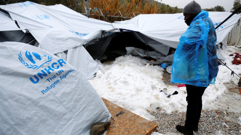 Un hombre trata de refugiarse del frío con un plástico en la isla griega de Lesbos. - REUTERS