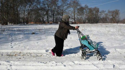 Una mujer empuja por la nieve el carro con su hijo en un campo de refugiados en Grecia. REUTERS