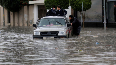 La gente empuja un vehículo a través de una calle inundada después de la lluvia en Trípoli/REUTERS