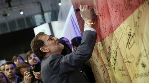 El presidente del Gobierno y líder del PP, Mariano Rajoy, firma en una bandera española a su llegada a la segunda jornada del XVIII Congreso nacional del partido en la Caja Mágica, en Madrid. EFE/Javier Lizón