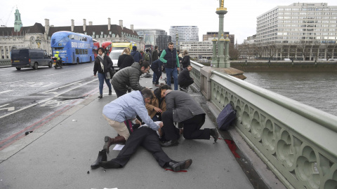 Varias personas atienden a uno de los heridos en el puente frente al Parlamento / REUTERS