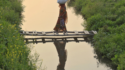 Una mujer agarra la mano de un niño mientras cruzan un puente hecho de bambú en un canal en Allahabad, India. REUTERS/Jitendra Prakash