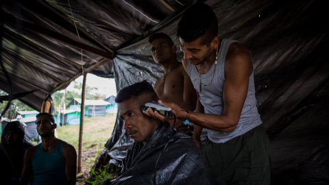 Un guerrillero le corta el pelo a otro mientras el resto ve una película en una carpa del campamento de desmobilizados de las FARC de La Fila, en la región de Tolima.- JAIRO VARGAS