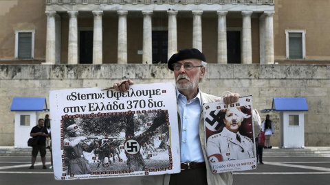 Un hombre sostiene un cartel de la canciller Angela Merkel como si fuera un miembro del partido nazi frente al Parlamento griego en la marcha por el Día de los Trabajadores en Atenas. /EFE