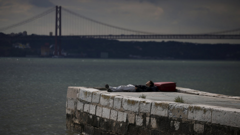 Un hombre duerme en una barandilla en el río Tajo en el centro de Lisboa. REUTERS