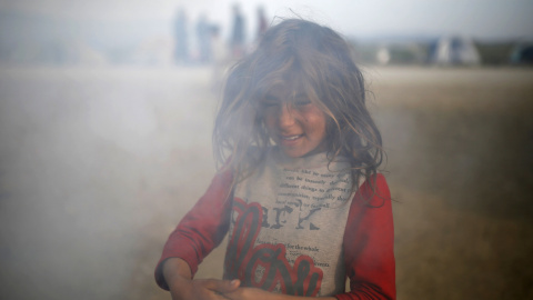 Una niña entre humo en un campamento improvisado para refugiados en la frontera entre Grecia y Macedonia, cerca de la localidad de Idomeni. REUTERS/Marko Djurica