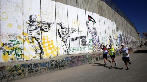 Participantes compiten junto al muro de separación durante la Maratón 'Derecho al Movimiento' en la ciudad cisjordana de Belén. Unas 4.300 personas han recorrido las calles de esta ciudad palestina durante la celebración de la cuarta carrer