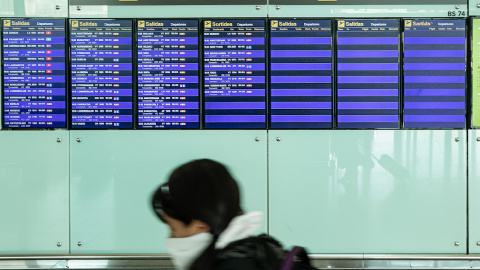 Una pasajera con mascarilla observa los paneles del aeropuerto El Prat de Barcelona, a 20 de marzo de 2020.