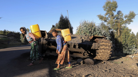 07/12/2021 Civiles pasan junto a un tanque militar destruido en los combates entre la Fuerza de Defensa Nacional de Etiopía (ENDF) y el TPLF