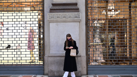 Una mujer con una máscara protectora mira su teléfono móvil mientras en un centro comercial cerca de la Piazza del Duomo, en Milán el 15 de marzo de 2021.