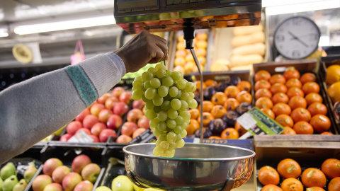 Un dependiente pesa un racimo de uvas en un mercado, a 31 de diciembre de 2023, en Madrid.