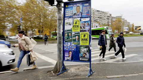 Una mujer pasa junto a un póster lleno de carteles electorales para las elecciones parlamentarias en Bucarest, Rumania.