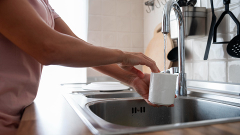 Una mujer llenando un vaso de agua en la pila de la cocina.