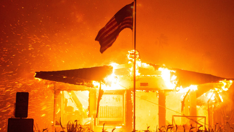 Una bandera estadounidense ondea mientras el fuego del incendio envuelve la estructura de una casa en el lado oeste de Los Ángeles, California, EE.UU.