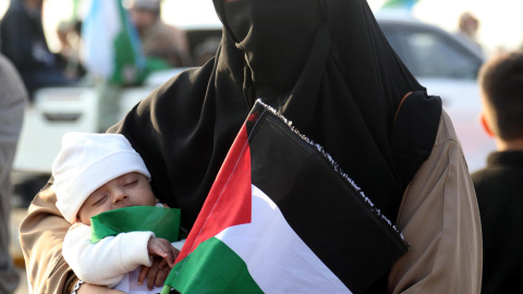 Una mujer sostiene a un bebé y una bandera palestina mientras los partidarios del partido político islámico Jamaat-e-Islami marchan para expresar solidaridad con el pueblo palestino, en Karachi, Pakistán.