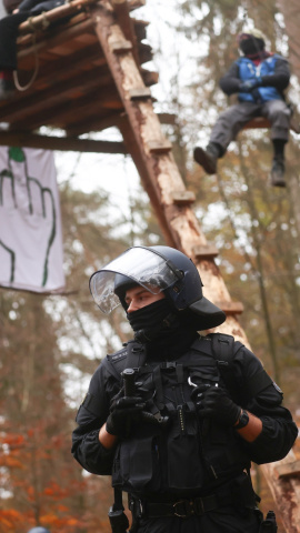 Un oficial de policía en la protesta contra la extensión de la autopista A49. Detrás un activista encaramado a los árboles.