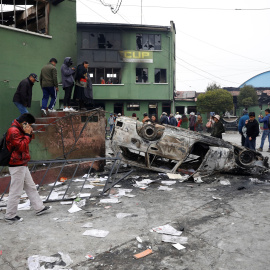 Ciudadanos caminan junto a un coche calcinado en El Alto, Bolivia. / Reuters