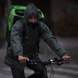 Un rider (repartidor) trabaja bajo la lluvia protegido con un impermeable, en Sevilla . E.P./María José López