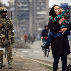  Una mujer sostiene y besa a un niño junto a soldados rusos en una calle de Mariupol el 12 de abril de 2022.- AFP