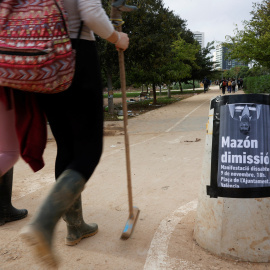 Dos voluntarios en las tareas de reconstrucción tras la DANA pasan junto a un cartel que llama a una manifestación en protesta por la gestión del president de la Generalitat Valenciana, Carlos Mazón, en València. REUTERS/Eva Manez