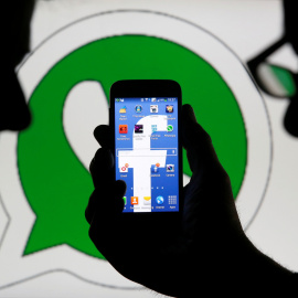 Foto que muestra un hom,bnre sosteniendo un móvil con el logo de Facebook en la pantalla, y detrás, el logo de logo de WhatsApp. REUTERS/Dado Ruvic