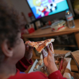 Un niño come un trozo de pizza del menú infantil de Telepizza mientras ve la televisión en su casa. EUROPA PRESS / JESÚS HELLÍN