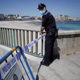 26/05/2020.- Un agente de la Policía Local de A Coruña delimita este martes con cinta policial una de las casetas de socorrismo que ha sido instalada en el paseo marítimo de la ciudad, a la altura de la coraza del Orzán en A Coruña. EFE/Cabalar