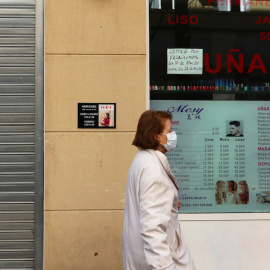 Una mujer usa una mascarilla mientras pasa por una peluquería cerrada propiedad de residentes chinos en Madrid. REUTERS / Sergio Perez