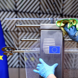 Un operario desinfecta un atril con la bandera de la UE, antes de la rueda de prensa del presidente del Consejo Eureopeo, Charles Michel. tras la primera cumbre de la UE en la se comenzaron a discutir el plan contra la crisis del coronavirus.. REUTERS/Fra