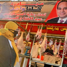 Una mujer con mascarilla camina frente a una carnicería con una pancarta del presidente egipcio, Abdel Fattah al-Sisi, en el mercado de Al Ataba, en El Cairo. - REUTERS