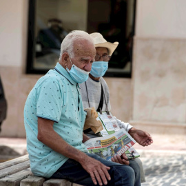 Una pareja de ancianos se protegen con mascarillas mientras descansan en un banco en Mahón, este jueves. | EFE