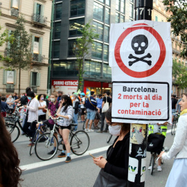 Primer pla d'un cartell que diu que la contaminació mata amb una manifestació contra els cotxes darrere, al centre de Barcelona. ACN / Pol Solà