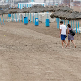 Una pareja pasea por la playa de la Malvarrosa en la que la afluencia de gente ha descendido notablemente debido en gran medida al descenso de temperaturas, a los chubascos y al cielo nublado. /EFE