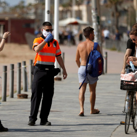 Agentes Civicos indican a una joven que se coloque la mascarilla protectora, este sábado en el paseo marítimo de la Barceloneta en Barcelona. EFE/Toni Albir