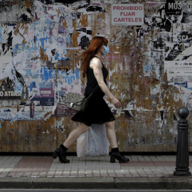 Una mujer con mascarilla camina este jueves por una céntrica calle de A Coruña, frente a un muro lleno de carteles con actividades culturales,en la jornada en la que ha entrado en vigor llevar este tipo de protección en espacios públicos, tanto al air