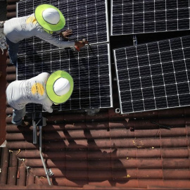 Dos operarios colocan paneles solares en el tejado de una vivienda. Foto: Joe Raedle / AFP