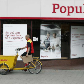 Un repartidor pasa ante una oficina del Banco Popular en el Paseo de Gracia esquina con la calle Aragón de Barcelona. | ANDREU DALMAU (EFE)