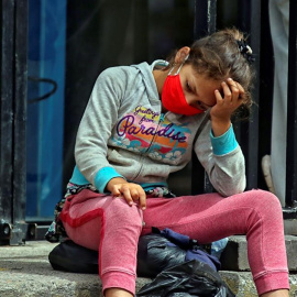 Una niña descansa en unas gradas mientras sus padres hacen fila para comprar alimentos. EFE/Gustavo Amador