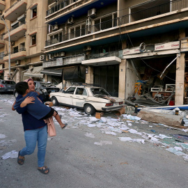 Una mujer lleva a un niño mientras pasa por las tiendas dañadas tras la explosión del martes en Beirut, Líbano