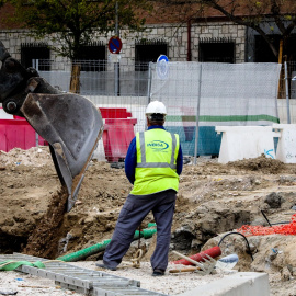 Dos trabajadores a pie de calle y otro en el tractor, en una obra en Madrid. E.P./Jesús Hellín