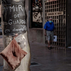 Una persona pasa ante la Consellería de Sanidad donde se puede ver una bolsa de basura usada a modo de bata con el lema "MIR de guardía ¿Te atiendo?". EFE/Biel Aliño