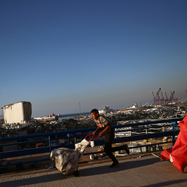 Jóvenes corriendo frente a los escombros de la explosión en el puerto de Beirut. / REUTERS