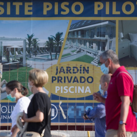 Varias personas caminan junto a un cartel de viviendas en venta en A Mariña (Lugo/Galicia). Carlos Castro / Europa Press / Archivo